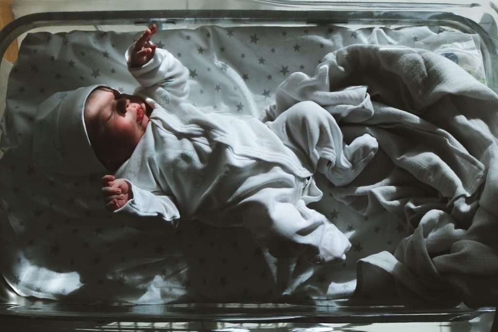 Newborn baby sleeping peacefully in a hospital bassinet cot with star-print sheets