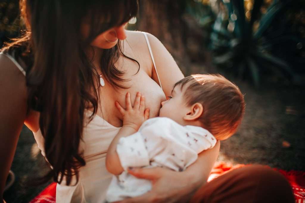 A mother breastfeeding her baby outdoors in warm natural light, representing confident and relaxed feeding.