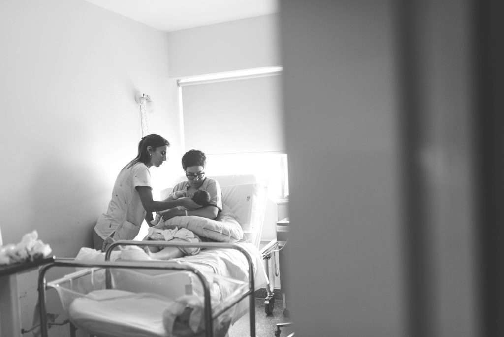 A nurse assisting a new mother with her newborn baby in a hospital room, representing lactation support services.
