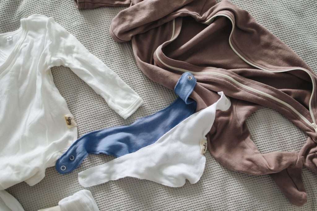 Newborn baby bodysuits and sleepsuits in white, blue and brown laid flat on a grey waffle bedspread