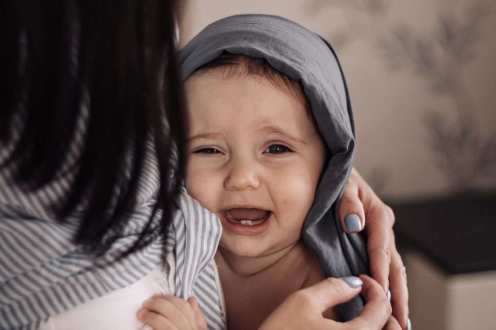 Crying baby showing teeth being comforted by parent - teething pain relief