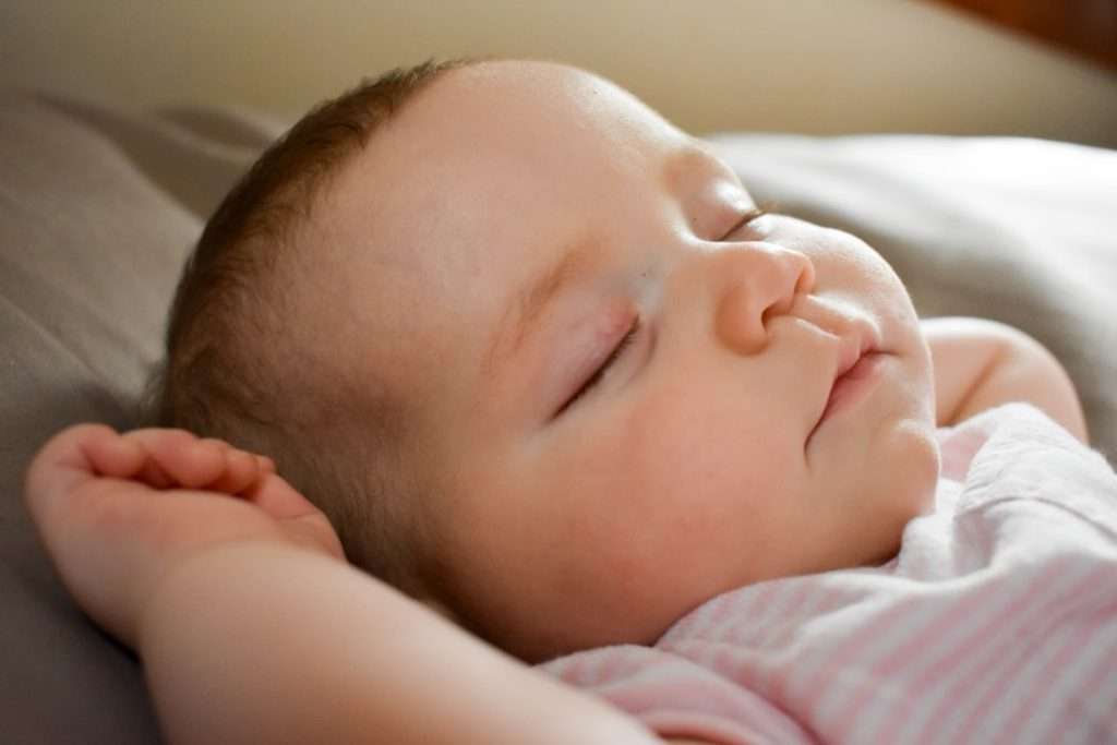 A newborn baby sleeping peacefully on their side, eyes closed. When evaluating co-sleeper features, prioritise those that support safe, uninterrupted sleep.