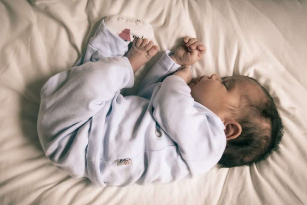Newborn baby lying on their back on a white surface, demonstrating the safe sleep position recommended by Plunket and the Ministry of Health NZ.
