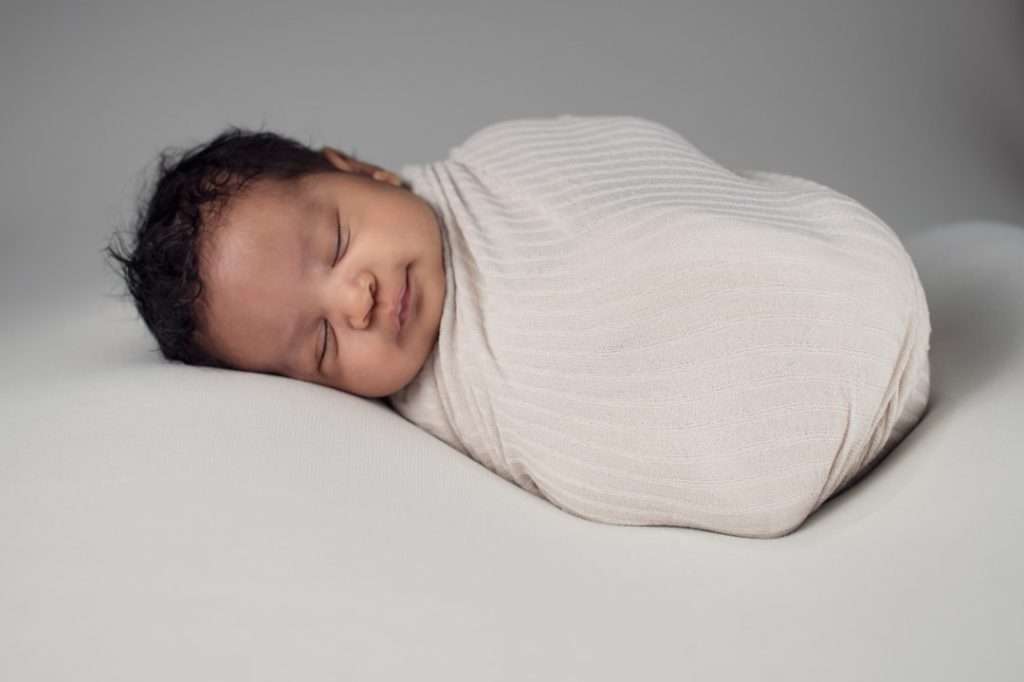 Newborn baby peacefully sleeping wrapped in a soft white muslin swaddle