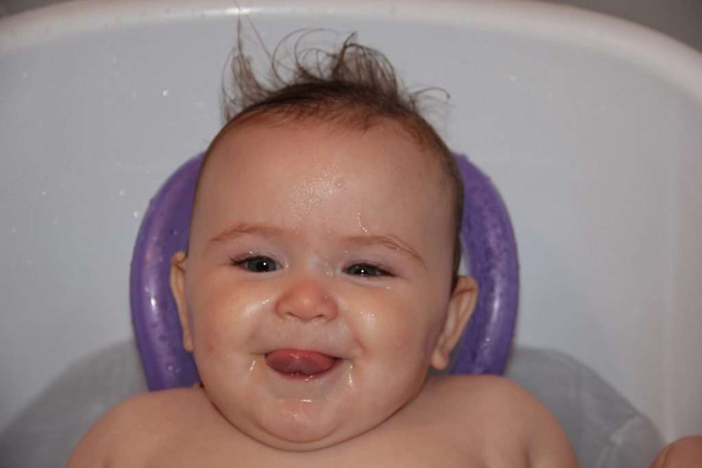 Happy baby sitting upright in a bath seat with purple side supports, showing a typical upright support seat in use