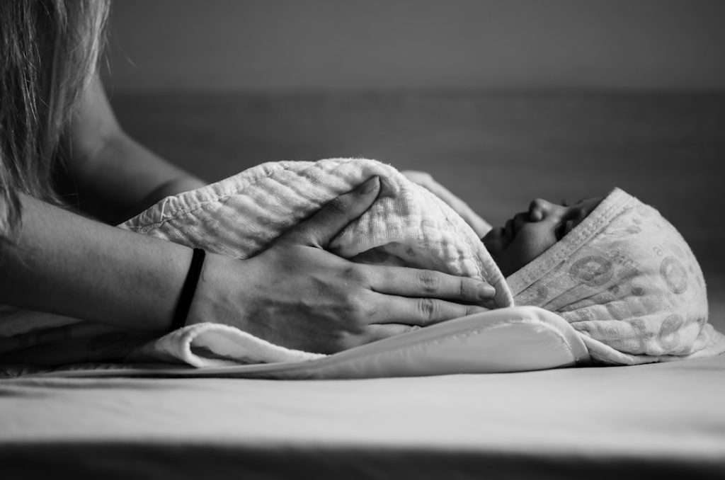 Parent's hands gently wrapping a newborn baby in a soft muslin swaddle cloth