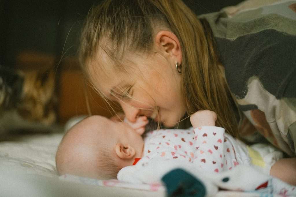A mother leans close to her newborn baby lying on a bed, representing the closeness a co-sleeper bassinet provides for night feeds. Photo by Unsplash.