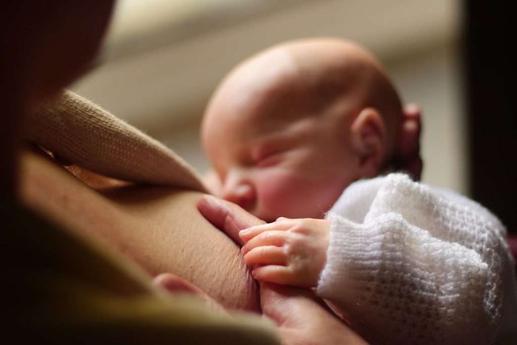 Close-up of a tiny newborn baby breastfeeding, cradled against their mother